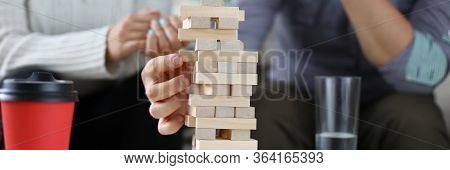 Close-up Of Male Hand Holding Wooden Block. Friends Playing Jenga And Spending Funny Time Together. 