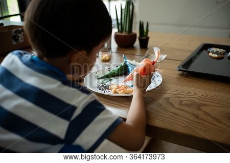Defocused Back Portrait Of Boy Decorating The Cookie Surface By Squeezing The Liquid Sugar