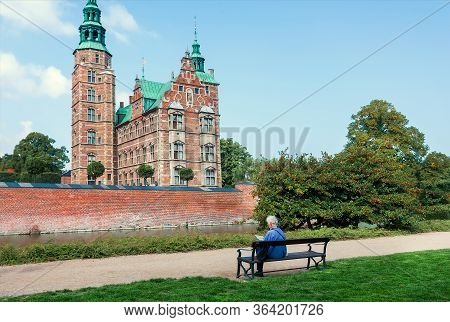 Lonely Person On Bench Near The Beautiful Towers Of Rosenborg Castle, Built In 17th Century In Copen
