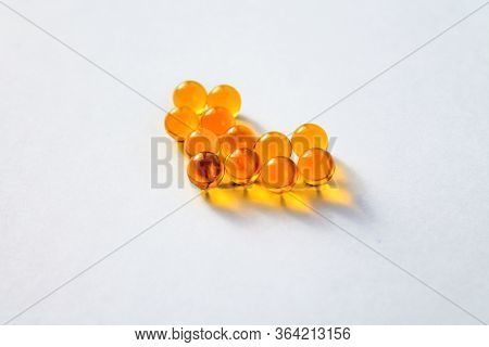 Yellow capsules of vitamins lie on a table on a white background in the shape of a heart