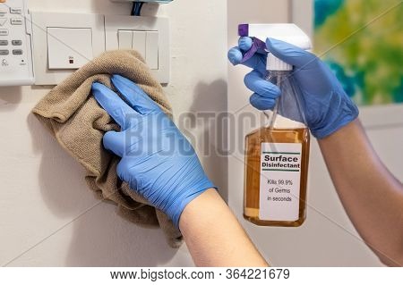 Person In Gloves Disinfecting Light Switch Panel Surface With Disinfectant Spray To Kill Germs, Bact