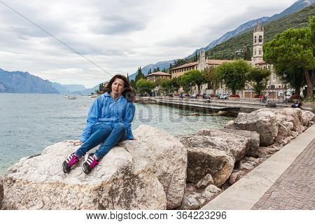 Castelletto, Italy, October 01, 2015 : Woman Sitting On A Stone At The Shores Of Lake Garda, Near Ca