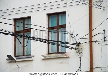 Many Tangled Electrical Wires Next To The Window And Wall Of An Old House. Problems Of Ill-conceived