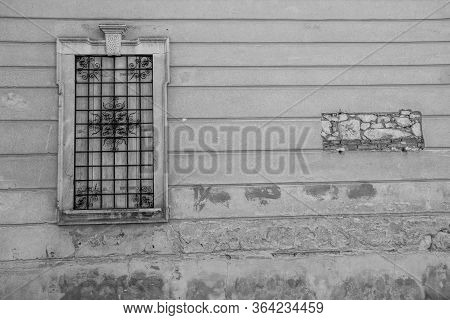 Closed Window With Wooden Shutters And Rusty Flower-shaped Grating And On The Wall The Place Of A Pl