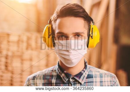 Portrait Of Confident Man Carpenter In Medical Face Mask And Hearing Protectors At Wooden Workshop. 