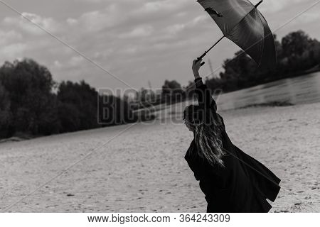 Woman In The Coat Walking With Umbrella On The River Bank