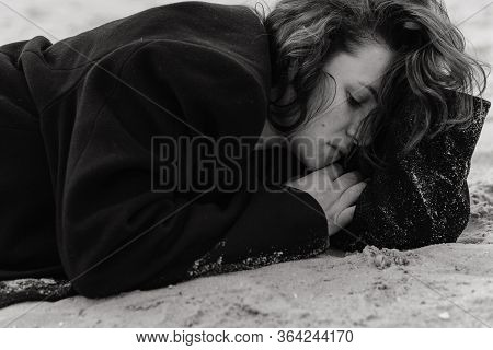 Curly Woman In The Coat Lying On The Sand