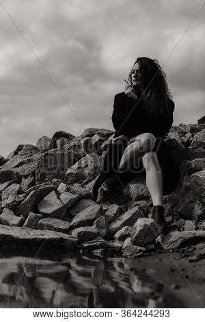 Woman In The Coat Sitting On The Stones And Smoking