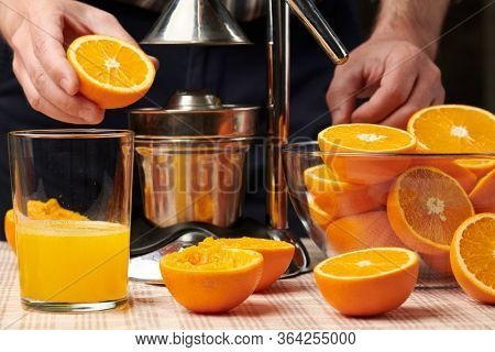 Squeezing an orange with a manual press, close view, making a glass of fresh. Fresh oranges on a wooden table, whole, squeezed and sliced.