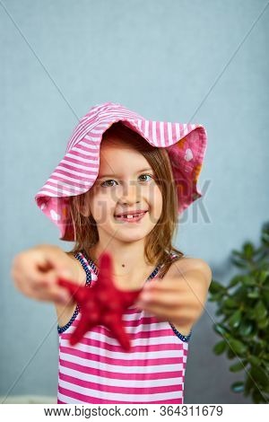 Smiling Little Girl Wearing Pink Hat Holding Starfish.