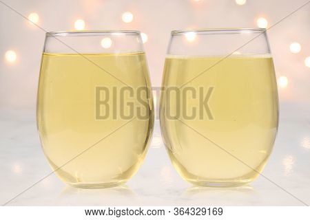 Two Stemless Wine Glasses Filled With White Wine On A Marble Background. White Lights Glow In The Ba