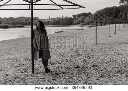 Woman In The Coat Standing Near The Metal Construction On The River Bank