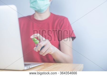 Asian Woman Wears Protective Mask Using Spray Alcohol Sanitizer Cleaning A Computer, To Prevent The