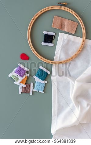 Embroidery tools on green background with wooden embroidery hoop, needles, needle threader and color