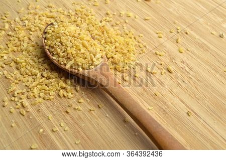Dry Cracked Wheat Daliya Grains In Wooden Spoon, On Bamboo Cutting Board