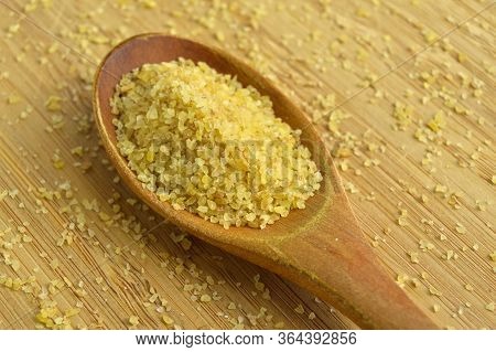 Dry Cracked Wheat Daliya Grains In Wooden Spoon, On Bamboo Cutting Board