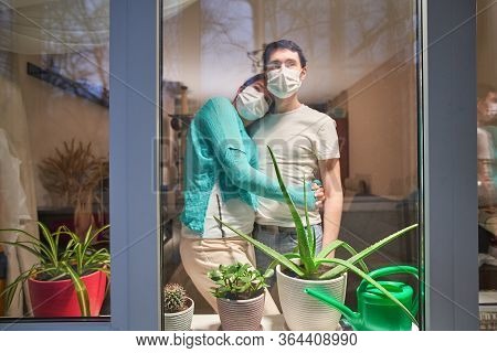 Man And Woman With Medical Mask On Their Faces Looking Through Window, Stay At Home, Selfisolation T