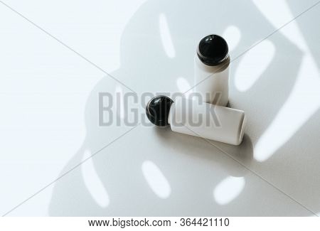 Two White Empty Plastic Bottles On A White Background With A Shadow Of A Tropical Leaf. Shampoo, Sho