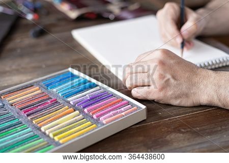 Person Painting With A Pastel Crayon Chalk On A White Sheet Of Paper With Pallette Of Pastel Chalks 