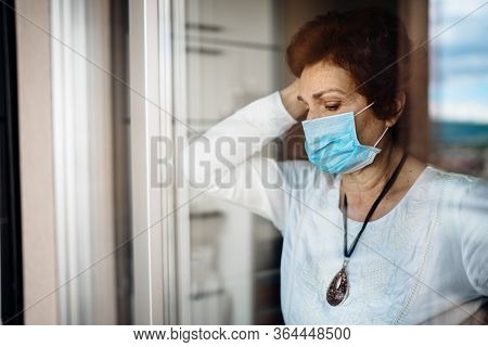 Senior Elderly Sad Woman At Home Looking Through The Window.coronavirus Covid-19 Disease Outbreak In