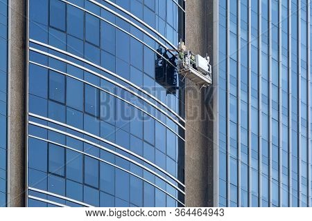 A Worker Washes The Glass Of A Multi-storey Building. Work On Cleaning Windows Of Skyscrapers In The
