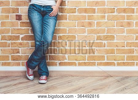 Woman Legs In Jeans And Red Sneakers, Woman Standing In Front Of Brick Wall, Fashion Concept
