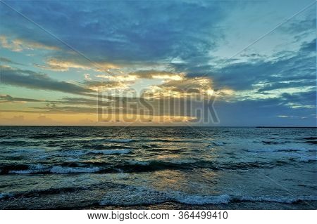 Sunset Over The Indian Ocean. Aquamarine Waves Slowly Rush Ashore. The Sky And Clouds Are Painted In