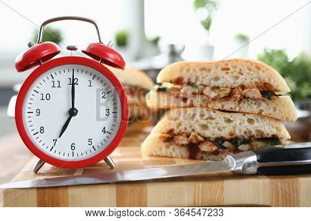 Close-up Of Red Clock Showing Seven In Morning. Hot Sandwich With Tasty Stuffing On Table. Quick Bre
