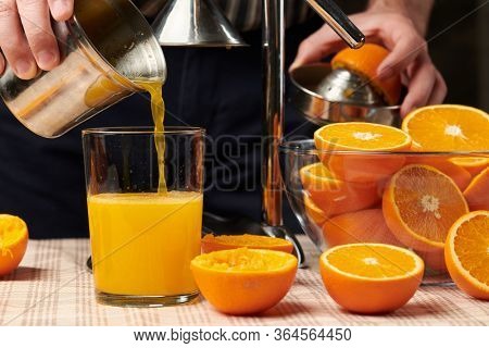 Squeezing an orange with a manual press, close view, making a glass of fresh. Fresh oranges on a wooden table, whole, squeezed and sliced.