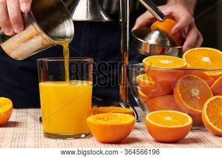 Squeezing an orange with a manual press, close view, making a glass of fresh. Fresh oranges on a wooden table, whole, squeezed and sliced.