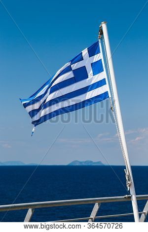 Greek Flag On The Blue Sky And Blue Sea Background At The Aft Of A Ferry Boat. Vertical.