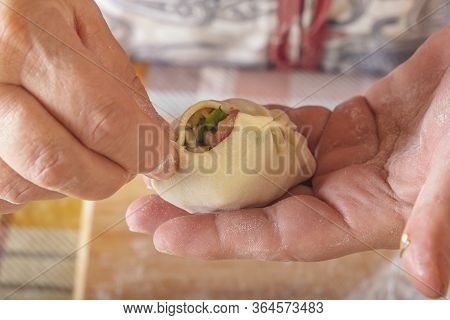 Female Hands Make Manti, Khinkali, Dumplings Or Wonton From Dough With Minced Meat Filling And Green