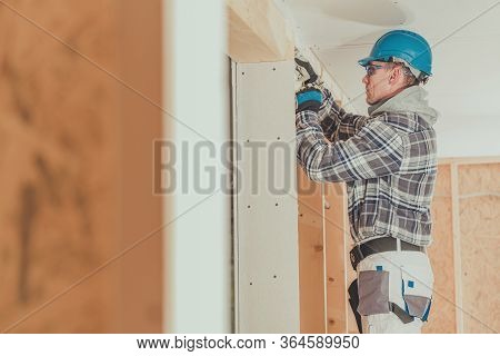 Male Electrician Contractor Feeding Electric Wire Through Wooden Framing In New House Construction.