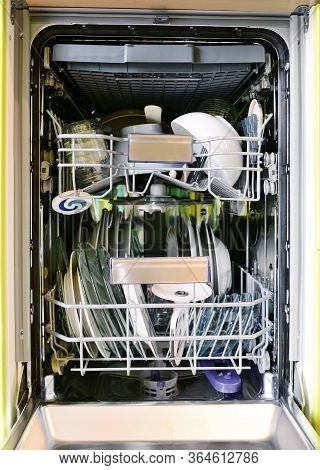 Front View Into Opened Dishwasher Full Loaded Of Dishes. Full Frame Background Shot.