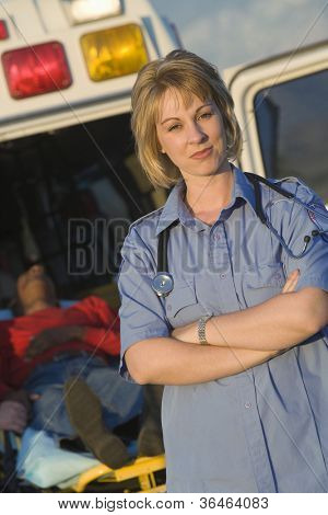 Portrait of a confident female EMT doctor standing with patient lying on stretcher in the background