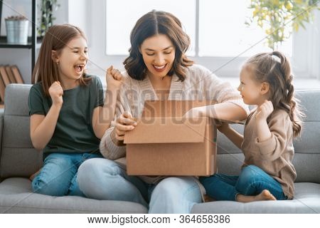 Mother and daughters are unpacking cardboard box at home.
