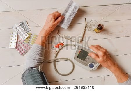 Senior Wrinkled Hand Pushing Back Pills And Thermometer, Dumb-bell On A Table. Another Old Woman Han