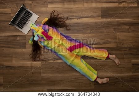 Top View Of A Girl In Unicorn Pajamas Looking At A Laptop, Lying On The Floor At Home
