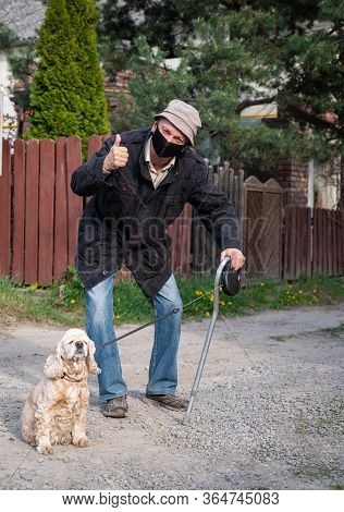 Senior Man In Protective Mask With A Cane Walking With A Dog In Sunny Day