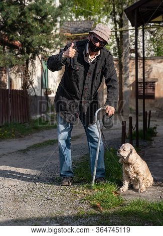 Senior Man In Protective Mask With A Cane Walking With A Dog In Sunny Day
