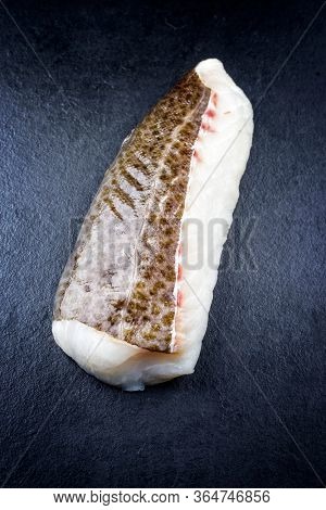 Raw Norwegian skrei cod fish filet with skin as closeup on black board with copy space
