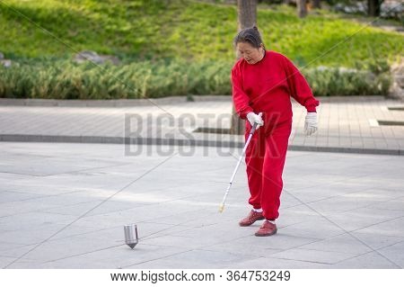 Beijing / China - April 3, 2016: Old Chinese Woman Whipping Spinning Tops, Traditional Chinese Game 