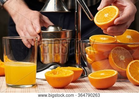 Squeezing an orange with a manual press, close view, making a glass of fresh. Fresh oranges on a wooden table, whole, squeezed and sliced.