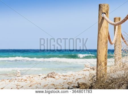 Rustic Fence With Wooden Poles And Rope On A Deserted Beach, In The Background The Rough Sea. Wild B