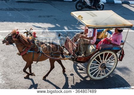 Port Benoa, Bali Indonesia -- Feb 28, 2016. A Horse Drawn Carriage And Driver Transports A Woman Pas