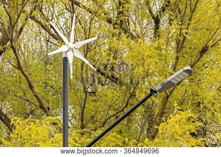 Street Electricity By A Small Windmill And Solapanels In City Against Buildings In Daytime. Concept 