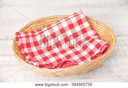 Wicker Basket With A Red Checked Cotton Napkin Inside On A White Wooden Table