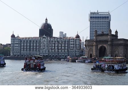 MUMBAI, INDIA - FEBRUARY 15, 2020: Taj Mahal hotel, Gateway of India and tourist boats in water of Arabian Sea on sunset in Mumbai, India
