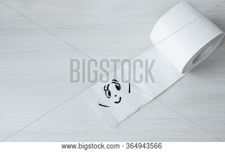 Toilet Paper With Funny Smiling Face On Wooden Background, Copyspace. Supplies For Quarantine Isolat