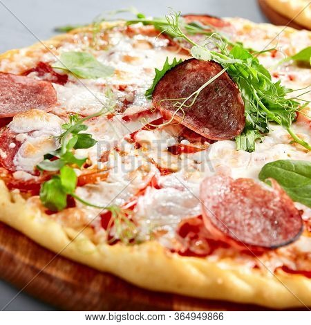 Prosciutto Funghi pizza on wooden board. Traditional italian cuisine bakery with salami, champignons, bell pepper, tomatoes, mozzarella and red tomato sauce close up. Hot snack, pizzeria meal